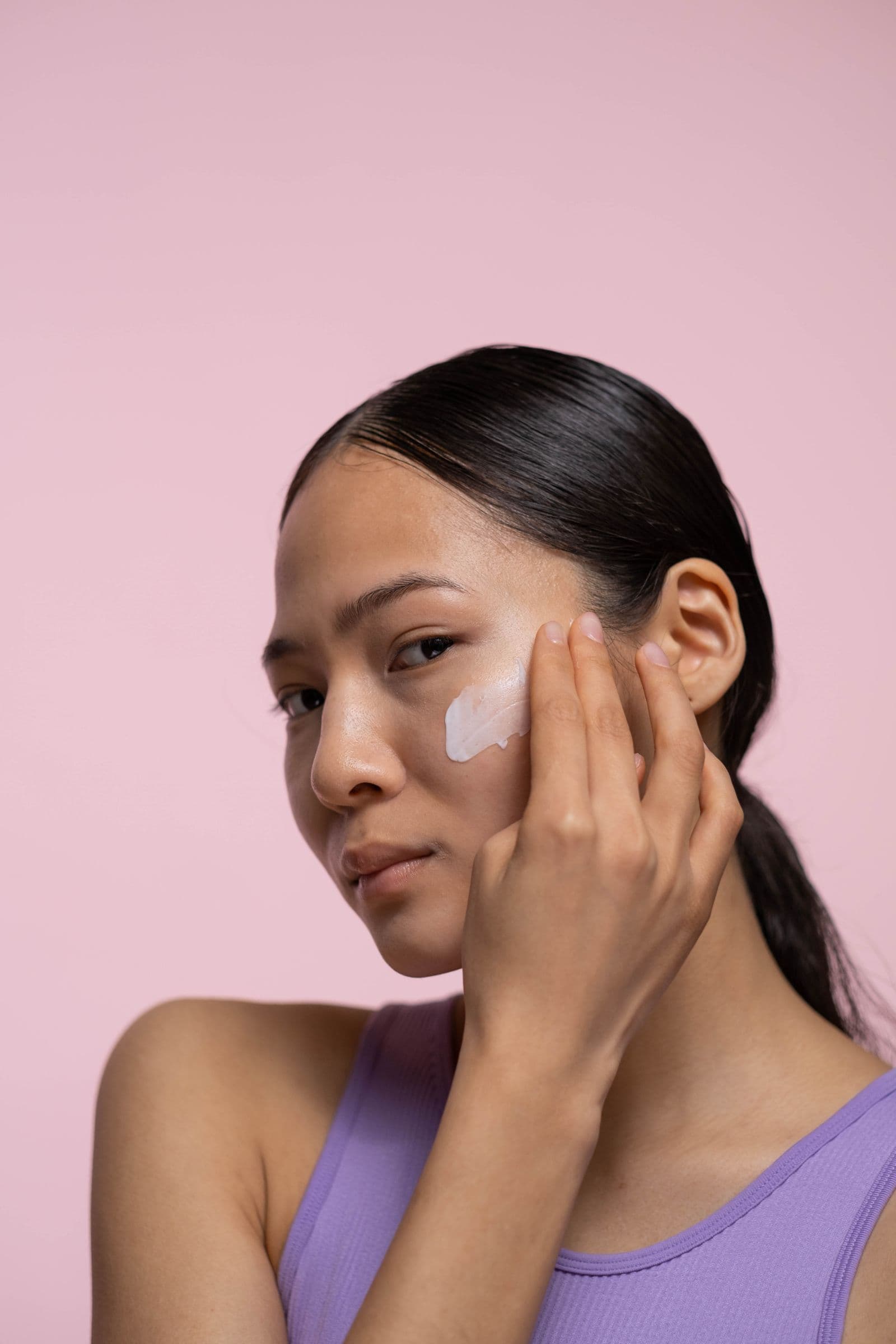 Mujer aplicándose skincare sobre fondo rosa Bella Beautiful